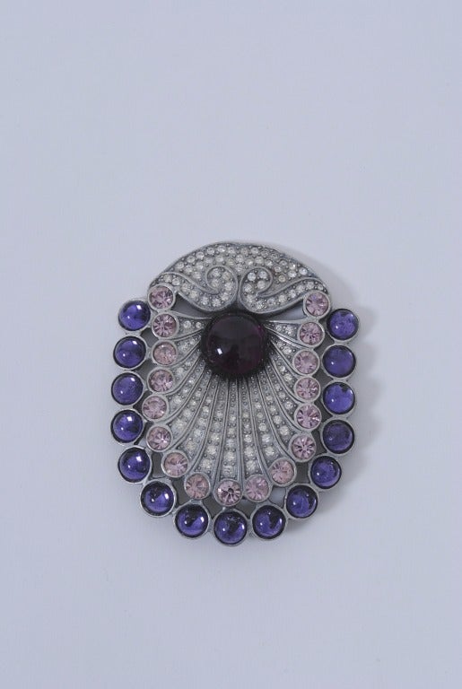 Beautiful large piece by Eisenberg of oval shape, the stones worked like spread peacock feathers and consisting of clear and pink crystals bordered by blue cabochons and with a deep purple cabochon at center, all set into a silver metal mount.