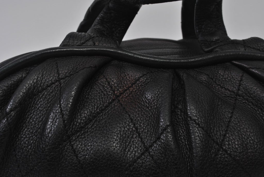 Chanel handbag in black caviar leather with large quilting pattern. Styled as a bowling bag with a shape that is long and rounded. The body is deep with a long central zipper and there are two flat leather loop handles on either side, where the