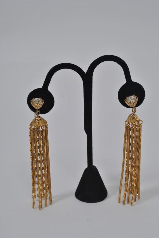 Shoulder ticking long earrings from Napier composed of several strand of gold chain interspersed with rhinestone chains, all suspended from a large round rhinestone in filigree setting faced upwards.