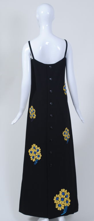 Make a dramatic entrance in this stunning Galanos dress. Simple, long and lean, the dress is emblazoned with clusters of embroidered yellow daisies with blue bead centers and sequin stems; these flowers graduate in size from the bust to the hem,