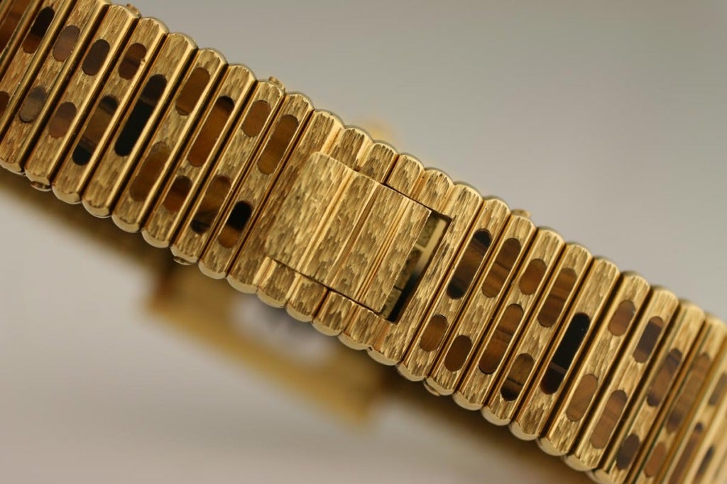 Piaget 18k yellow gold and tiger's eye lady's watch with integrated flexible link bracelet. The tiger's eye dial has no markers, yellow gold dauphine hands. The case measures 25mm square and the total length of bracelet is 7 1/2 inches.