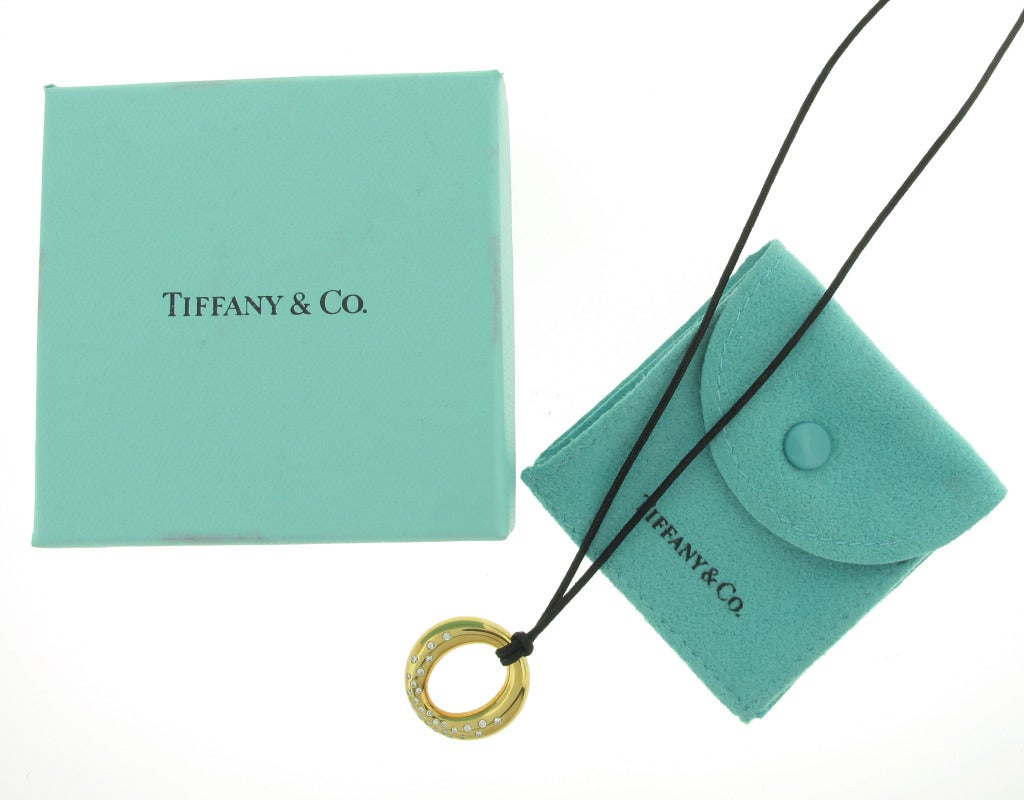 This Tiffany & Co. Sevillana pendant is in 18 karat yellow gold and features 26 round diamonds with at total weight of .37 carats. The circular pendant is just under an inch in both length and width. The black cord that the pendant hangs from