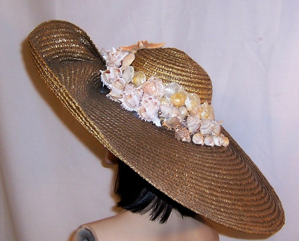 Offered for sale is this unusual and unique, one-of-a-kind, large metallic gold beach hat which has been embellished with a variety of sea shells and a singular starfish at the front and center of its crown.  The hat measures approximately 25