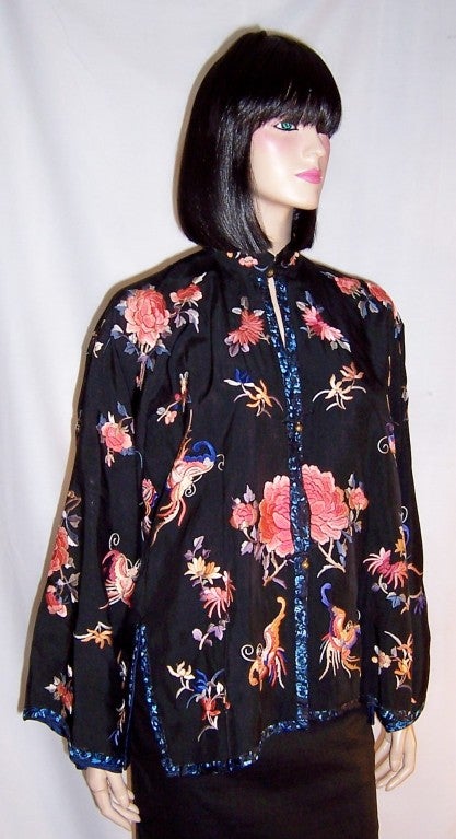 This is a charming black silk, 20th century, Chinese embroidered jacket with coral peonies,  peony buds, and butterflies.  The jacket is trimmed in black and blue floral embroidered trim.  It has three brass metal buttons for closure and a navy blue