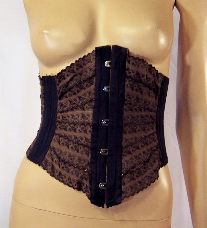 This is an unusual Victorian brown and black, underbust waist cincher.  The back is black elastic and has been fitted with a series of holes on each side for ties or laces to be inserted to make the cincher looser or tighter. The front and sides of