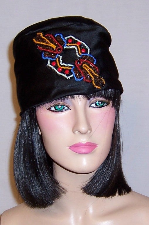 This is a wonderful custom-made, 1920's vintage, black silk toque hat which has been embellished with a multi-colored beaded element at its front and center.  Toques were always close-fitting and brimless.  This one is fully lined in silk and has