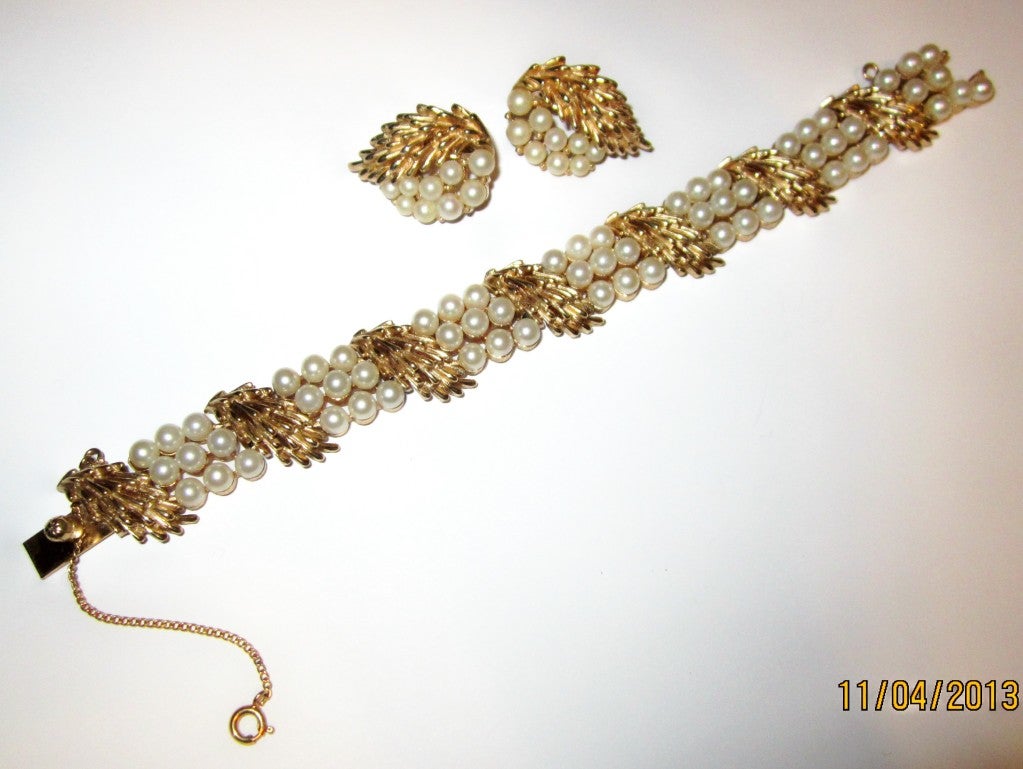 This is a striking Trifari gold-tone and faux pearl bracelet with a safety chain and earring set in excellent vintage condition.  The bracelet has three rows of pearls separated by seven stylized leaf elements and measures 7
