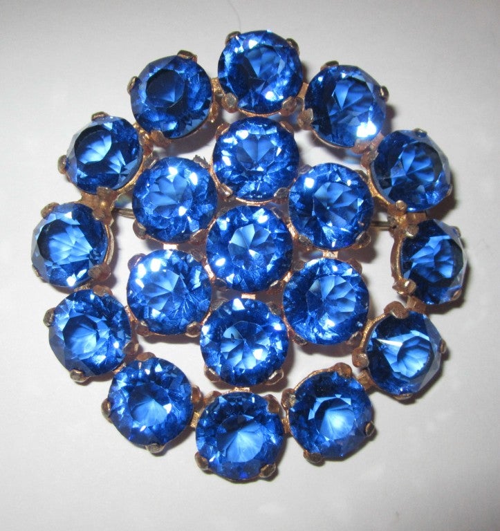 This is an eye-catching large rounded brooch with large cobalt blue cut crystal stones surrounding a center of 7 additional large stones. Its diameter measures 2.25