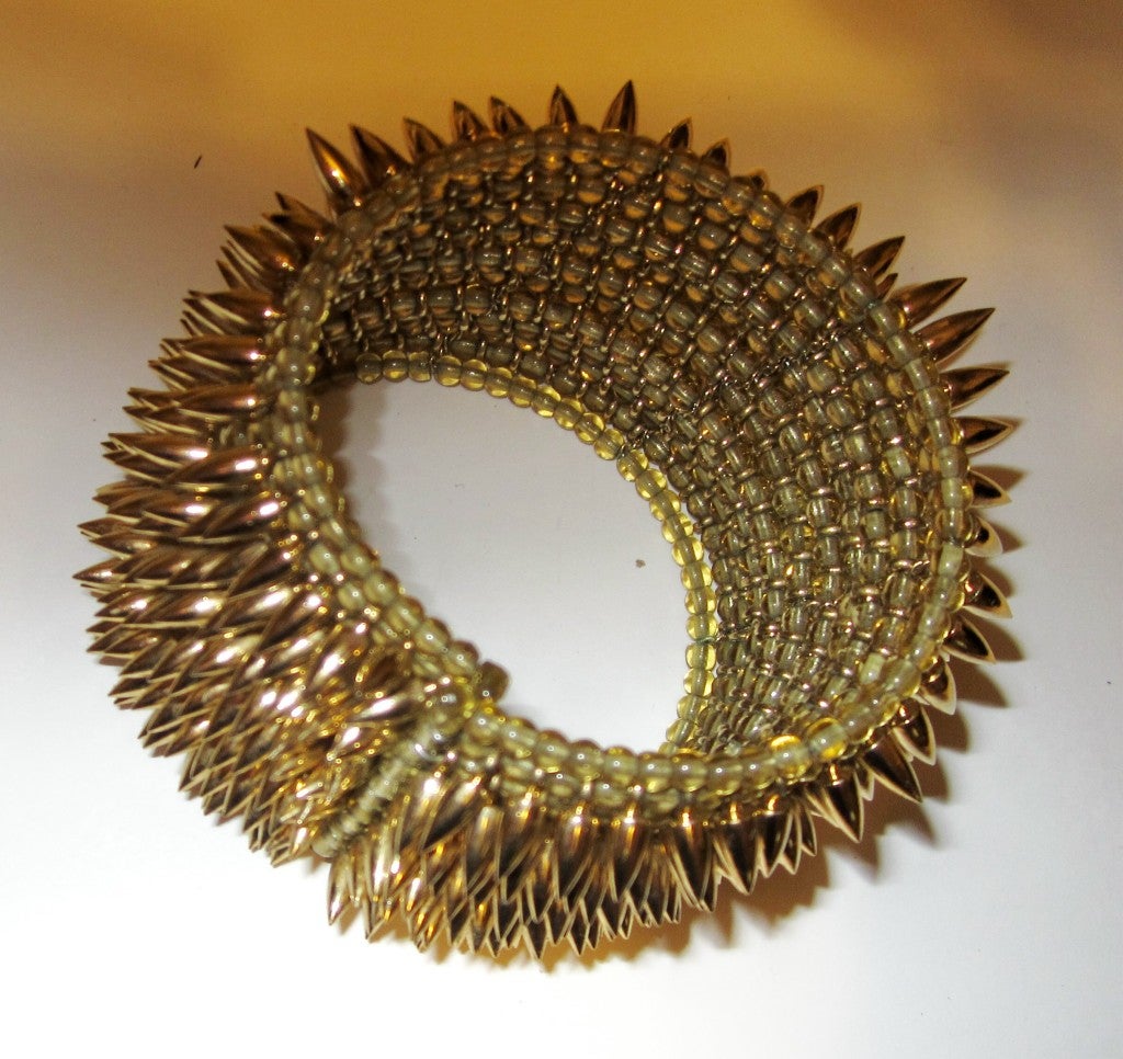 This is an unusual cuff bracelet designed by Jessica Rose, consisting of 10 rows of yellow glass beads interspersed with 10 rows of brass colored spikes.   It measures 1.75