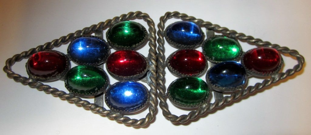 This is a striking Art Deco belt buckle consisting of two triangles hinged together.  Each triangle consists of 6 brightly colored cabochon glass stones in red, green, and cobalt blue.  The belt buckle measures 5.5