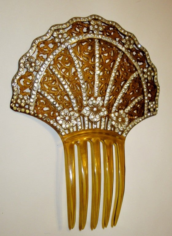 This is a stunning Art Deco amber-colored celluloid comb in the typical fan-shape embellished with filigree work and rhinestones throughout the design.  It measures 5