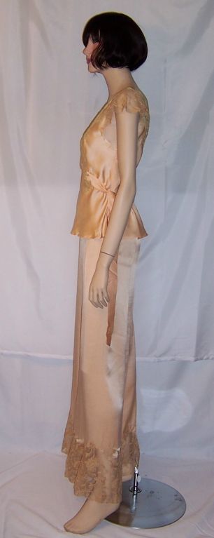 This is a glamorous, 1930's vintage, pale apricot silk pajamas/lounging set trimmed in ecru lace. The bottoms have tiny pearlized buttons for closure on the left side. The top must be slipped over the head to be worn, has attached belt, is also