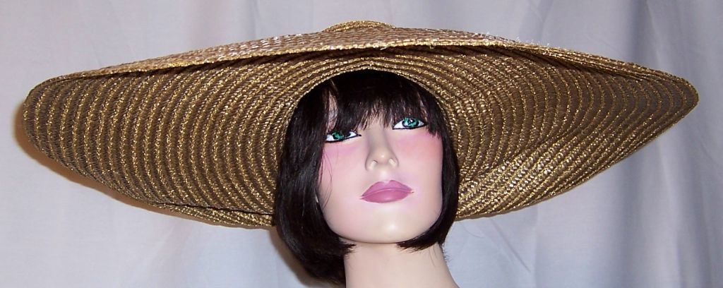 Offered for sale is this 1980's, oversized tan straw hat with gold metallic thread trim and a shell motif in the center and back of the crown of the hat. The brim measures 9
