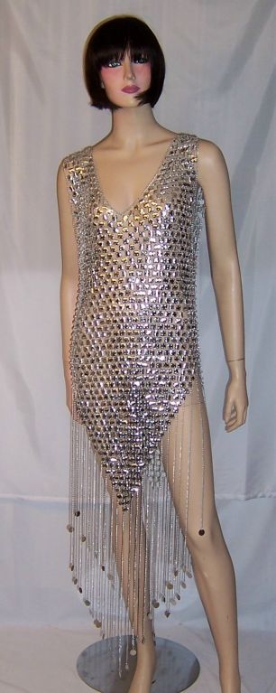 This is a wonderful 1960's sleeveless, tunic-type dress, hand-assembled, with tiny, plastic square-shaped pieces connected with metal jump rings and long metal fringe each terminating with a round metallic disk. The dress is elegant and