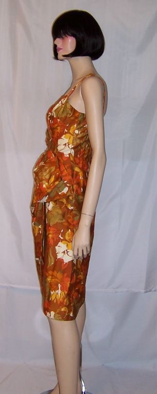 This is a striking, 1940's vintage, floral printed sarong in rust, orange, gold, green, and white. The colors are vivid and exotic and the design is stylish and dramatic. The bodice is tightly fitted with some asymmetrical pleating and the fabric