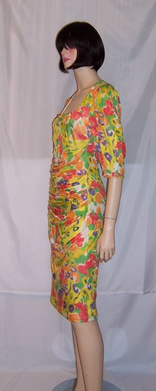 This is a bright and vibrant floral printed silk dress is springtime hues of yellow, orange, green, and violet designed by Emanuel Ungaro for his ready-to-wear collection. The dress is marked a size 38/12, but is more comparable to a size 6. In the