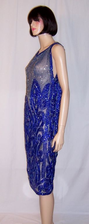 This is a stunning and elaborately hand-beaded cobalt blue and silver flapper dress on blue net in stylized Art Deco design patterns. The dress is equivalent to a size 6/8 and is very good to excellent vintage condition.