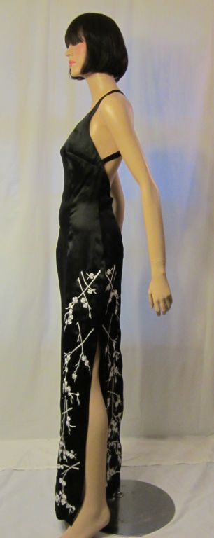 This is a striking, black and white embroidered evening gown designed by Nicole Miller in 100% silk. It is reminiscent of the cheongsams of the 1950's with its sleek silhouette,  embroidered plum blossoms, and slit up the side of the gown. The gown