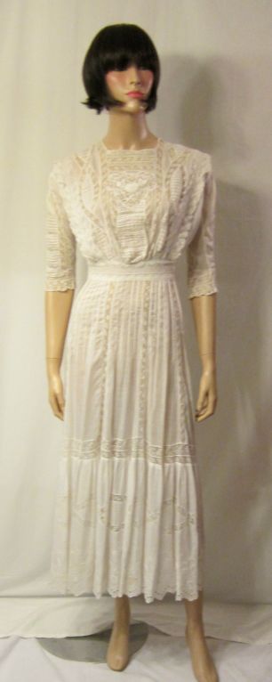 This is a lovely white Edwardian tea gown with hand-embroidery and lace inserts. The gown has a combination of tiny pearlized buttons and hooks and eyes for closure down the back, 3/4 length sleeves, and would be comparable to a size 6 or Small. It