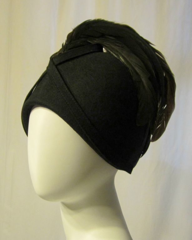 This is a dramatic black woolen helmet hat decorated with wonderful coque feathers from the front and center of the hat to the back of the hat. Its circumference measures 22