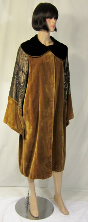 This is a strikingly beautiful deep ochre-colored silk velvet opera coat with black and gold lame sleeves and side panel inserts. The coat has one fabric covered button at the neckline for closure. The collar is two-toned, black and deep ochre, and
