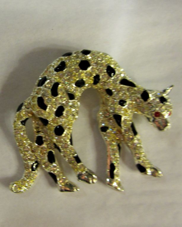 This is a stunning clear rhinestone leopard brooch with black enameled accents and red rhinestone eyes. The brooch is stamped on the reverse side in the silver-toned metal, however, it is not clearly distinguishable to me. The brooch measures 2