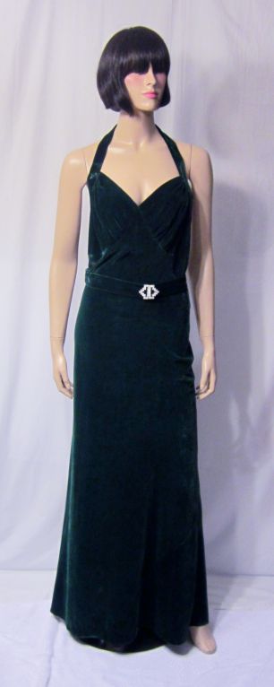 This is an elegant and sensuous 1930's bias-cut, emerald green velvet gown with a halter neckline, low-cut back, and snaps on the left side for closure. The belt has an Art Deco rhinestone buckle attached and the belt can be twisted for a more
