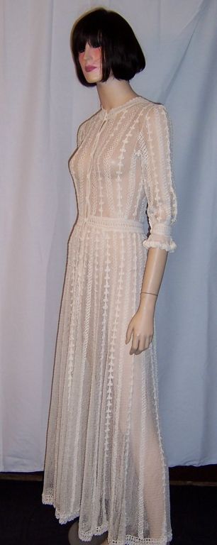 This is an exceptionally fine white lace crocheted gown with beautiful details. It has a series of fabric covered buttons from the neckline to the hemline. The sleeves are elbow length with a ruffled edge and a fabric covered button on each sleeve.