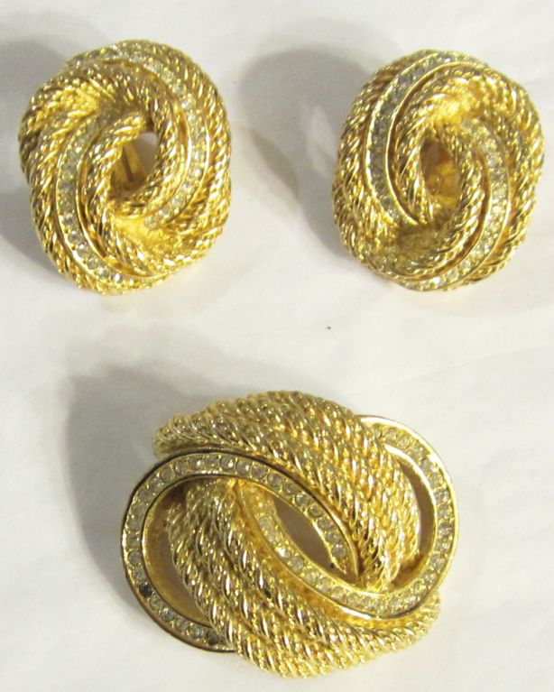 This is a striking gold-toned textured brooch in a stylized knot formation with a string of clear rhinestones encircling the gold-toned rope. The singular dark spot is not a missing rhinestone but rather a 