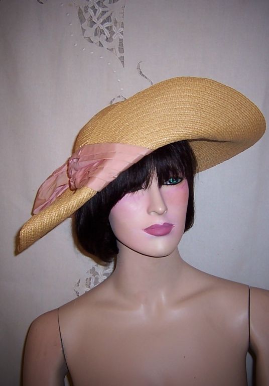 This is an original very fine natural colored straw hat wrapped in thick, pale pink silk ribbon with a large bow on the side. The design shows the extraordinary talents of the milliner in the manipulation of the straw. Jay Thorpe's department