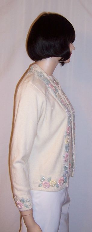 Offered for sale is this early 1960's white beaded twin sweater set made of angora, lamb's wool, and nylon. The elaborate beadwork has been masterfully created into three dimensional floral designs with pale blue, pink, and pale yellow flowers with