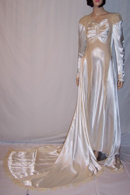 Offered for sale is this exquisitely designed, 1940's vintage,

white charmeuse wedding gown with a long and full train, embellished with ecru embroidered lace insertions and trim. The bodice is ruched in the center resembling a butterfly and is
