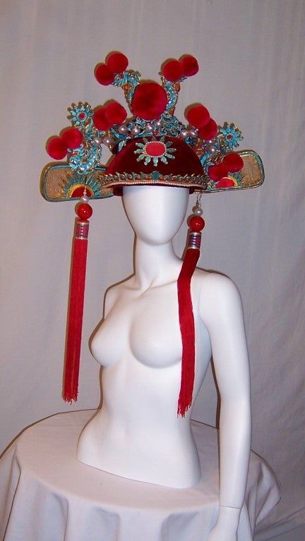 This is an elaborately decorated vintage, probably dating to the 1970's-1980's, Chinese theater hat which is comprised of seven pieces and must be assembled. The base of the hat is made of cardboard and covered in deep red velvet. Another section of