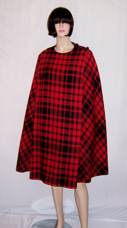 This is a striking, 1960's vintage, black and red plaid cape and matching skirt ensemble. The cape's popularity surged during the 1960's and just about every fashionable woman had at least one in her wardrobe. This cape has two black ball-shaped