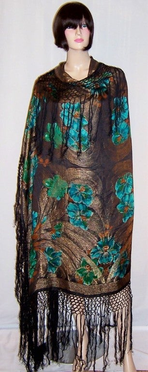 This is a strikingly vibrant 1920's Art Deco shawl depicting daffodils in viridian green and thallo blue with deep yellow ochre centers in a very painterly fashion on a black and gold lame background with long black fringe. The shawl measures 48
