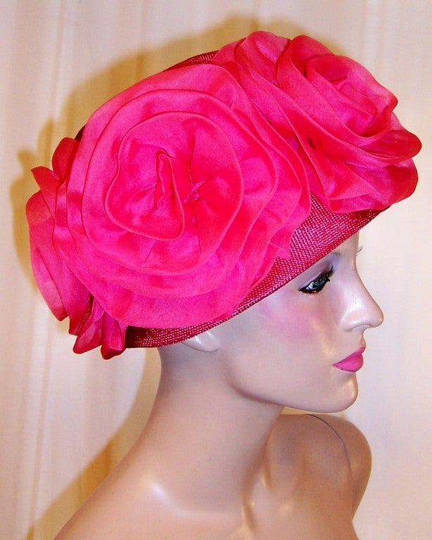 This is a stunning, shocking pink chapeau whose frame is made from fine straw and whose crown is encircled with five oversized organza blossoms.  The hat is in excellent vintage condition and its circumference measures approximately 22