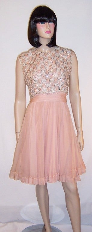 This is a fabulous and flirty 1960's silk chiffon cocktail dress with a sleeveless, elaborately decorated bodice of crystals, rhinestones, and tiny strips of pink velvet ribbon. There are approximately five tiny loops of crystals missing, but they