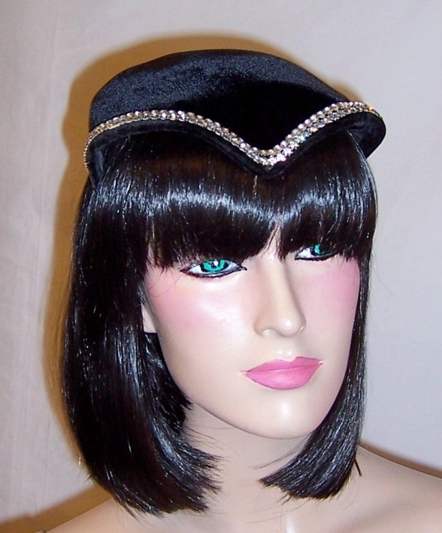 This is a simple and chic Art Deco black velvet chapeau embellished with a stunning rhinestone trim accentuating the entire shape of the hat. No label is present, the hat is in excellent vintage condition, and would comfortably accommodate most head