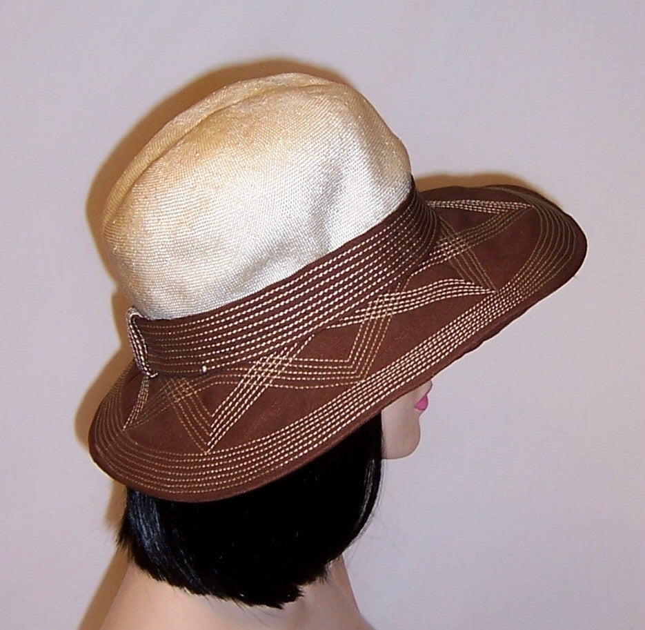 This is a chic and sophisticated summertime wide-brimmed hat made of fine white straw and cocoa brown fabric whose brim and band around its crown has been embellished with meticulous trapunto stitching.  The hat has been styled by Nadelle of