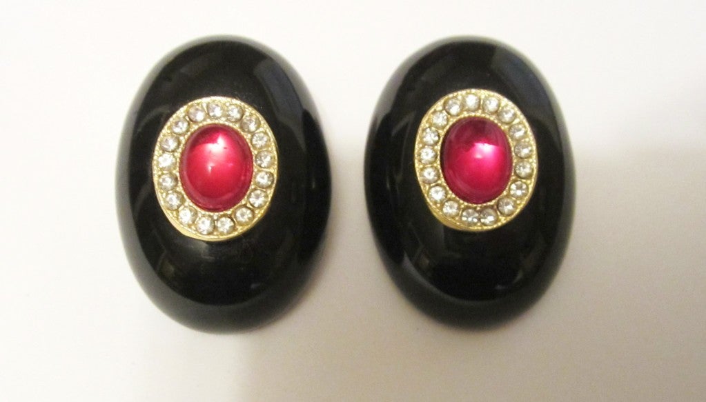 This is a striking pair of Italian, black bakelite-like, resin clip-on earrings, oval in shape, embellished with a red oval cabachon stone and surrounded by tiny rhinestones in a gold-toned mounting.  The earrings are in excellent, unworn vintage