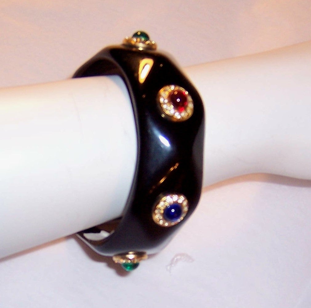 This is a beautifully made 1980's Italian black, bakelite-like, resin plastic bangle with no seams and decorated with small cabachon stones in red, blue, and green surrounded by tiny rhinestones in gold-toned mountings.  The bracelet is in excellent
