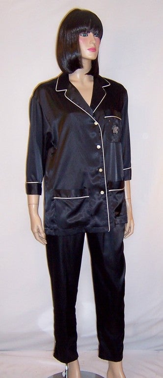 This is a simple and stunning pair of black satin pajamas trimmed in white, designed by Calvin Klein. The top has 3/4 length sleeves, four buttons for closure, and three pockets. The top pocket has the CK monogram in white.  The pants are pull-ons