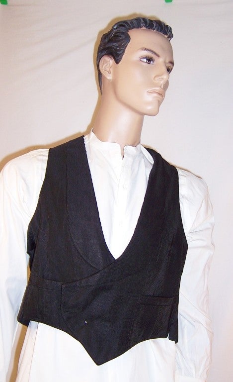 This is a handsome Edwardian (1901-1919) black silk, bedford corded waistcoat. Bedford cord is fabric distinctfully woven to create a lengthwise corded or ridged effect. The vest is in very good condition with some minor fraying at the right upper