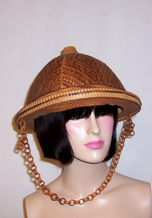 This is an unusual and rare Asian helmet hat made of bamboo with a banana leaf interior whose anonymous designer masterfully created with the most inticate design details.  The crown is covered in dark and light  interwoven diamond-shaped patterns