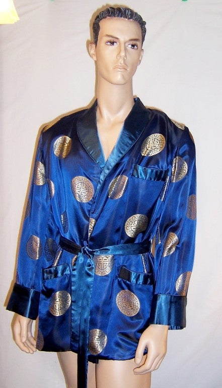 This is a stunning, 1950's vintage, men's cobalt blue brocaded smoking jacket with repeated Asian symbols throughout the design by Monet LTD. of Hong Kong.  The smoking jacket has a shawl collar, three pockets, large cuffs, and a detachable belt. It