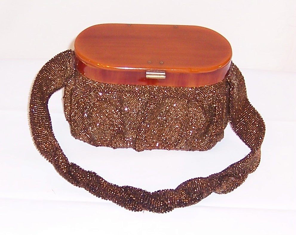 This is a striking, 1940's vintage, bronze colored beaded, oval-shaped bag with a bakelite lid and frame, a satin lining, and a heavy partially twisted handle. The bag measures 5