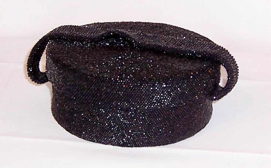 This is a simple and dramatic, 1940's vintage, black glass beaded, hat box shaped evening bag with a wide beaded handle, lined in black satin with a zippered compartment and a mirror. The bag measures 6 3/4