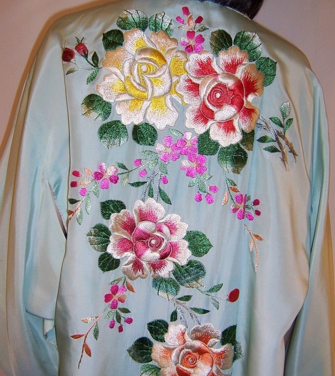 This is a lovely and luxurious mint green silk, Japanese hand-embroidered kimono depicting large roses, plum blossoms, a pagoda and possibly Mount Fugi in hues of yellow, red, pink, apricot, blue and green.  This mid-twentieth century kimono is in