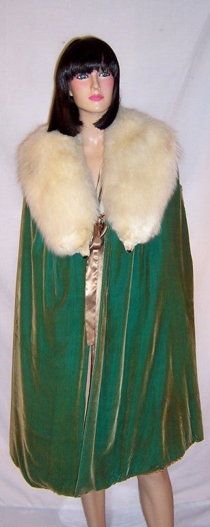 This is an extraordinarily beautiful 1920's green silk velvet cape with a huge white fox collar that accentuates the cape and frames the face.  Each shoulder is embellished with two curved, three dimensional lines of ruched or woven fabric which