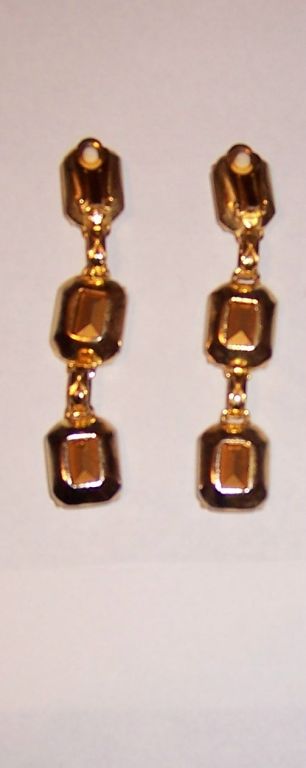 This is an eye-catching pair of long dangle, clip-on earrings of the 1980's vintage. Each earring is comprised of three large, rectangular-cut clear rhinestones with gold foil backing connected by a gold-toned rope finding. Each earring measures